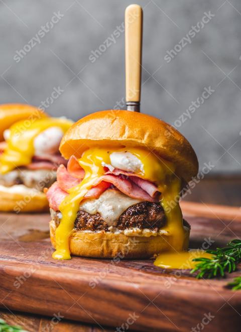 Mouthwatering burger topped with gooey egg and ham on a wooden board