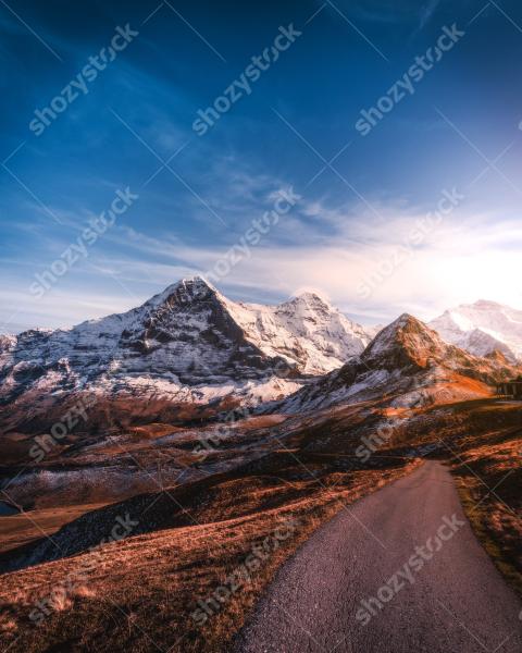 Snow-capped mountains view during golden hour with winding path in the foreground