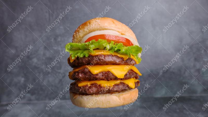 Delicious triple cheeseburger with fresh lettuce and tomato on a rustic background