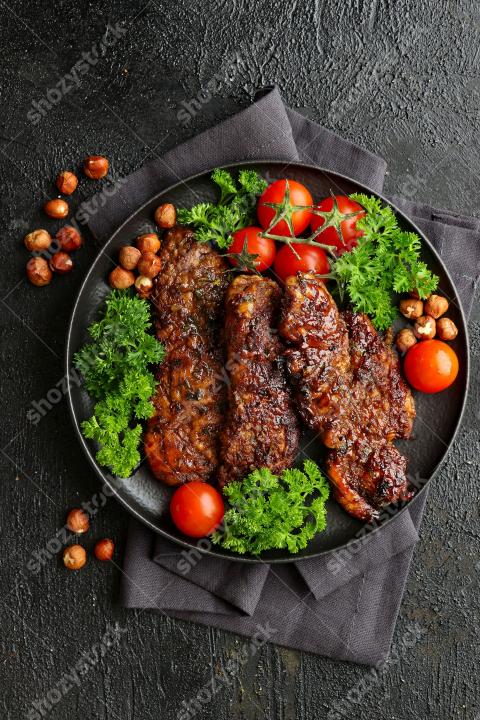 Grilled meat served on a black plate with fresh greens and cherry tomatoes at a dining table